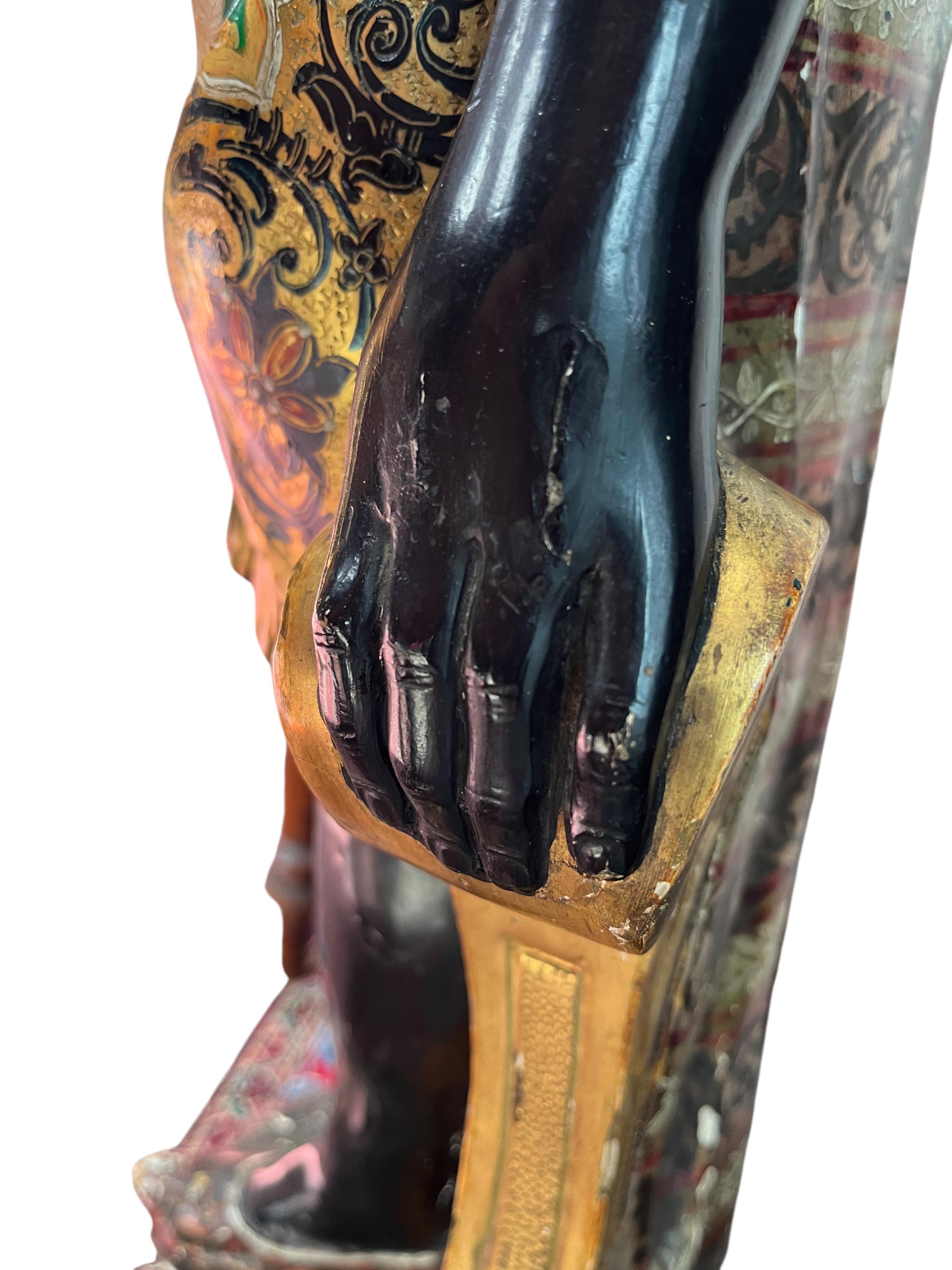 A 19th century Italian carved wood and composition polychrome painted blackamoor torchere, modelled standing with one arm holding a scroll pillar on waisted circular base and lions paw feet, 106cm high